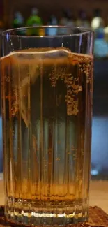 A chilled drink in a tall glass with ice and bubbles on a bar counter.