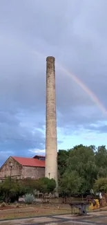 Historical chimney with rainbow in cloudy sky.