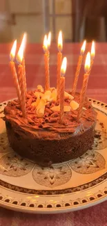 Chocolate cake with lit candles on a patterned plate.