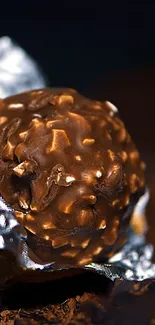 Dark chocolate truffle with a rich texture, wrapped in silver foil on a dark background.