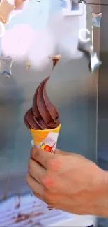 Hand holding chocolate ice cream cone by dessert machine.
