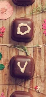 Chocolate candies spelling 'Love' with flowers on wood.