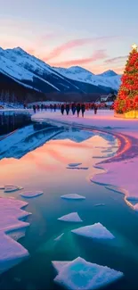 Christmas tree by a snowy lake with mountain backdrop at sunset.