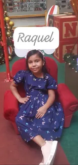 Christmas themed wallpaper with girl in blue dress on red chair.