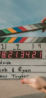 Film clapperboard held by hand under blue sky.