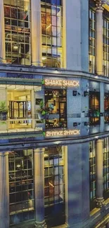 Reflective cityscape at night with illuminated building facade.