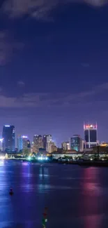 Vibrant city skyline at night with river reflections and glowing urban lights.