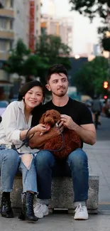 Couple with dog sitting on a city street in the evening.