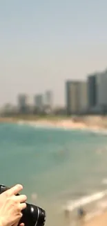 Mobile wallpaper of a cityscape and beach scene with a photographer's hands.