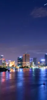 Cityscape at night with river reflections and a starry sky.