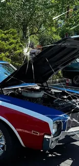 Classic red and blue American muscle car with open hood at a car show.