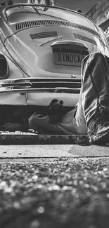 Monochrome image of a mechanic under a vintage car in a garage workshop.