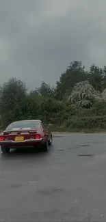 Red classic car driving through scenic countryside on overcast day.