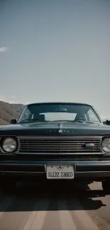 Front view of a classic black car on a scenic road with a mountain backdrop.