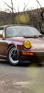 Vintage Porsche driving on a scenic road with burgundy hues.