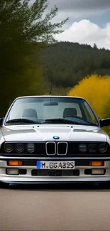 Classic car on scenic road with green trees.