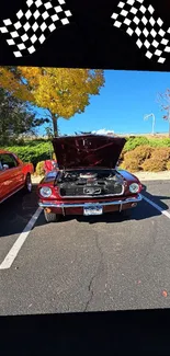 Classic red car with hood up under checkered flags in an autumn setting.