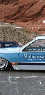 Vintage blue racing car with desert rocks in background.