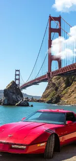 Red classic car parked by Golden Gate Bridge under blue sky.