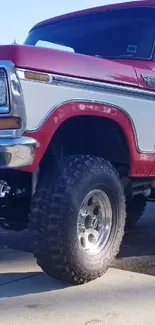 Close-up of a classic red and white off-road truck with rugged tires.