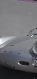 Classic silver car against a concrete wall, showcasing retro design elegance.