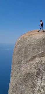 Person walking on a cliff edge with a vast sky and ocean backdrop.