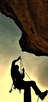 Silhouette of climber against sunrise sky hanging from rock.