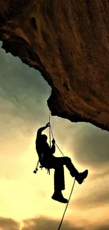 Climber silhouette against golden sunset on rocky cliff.