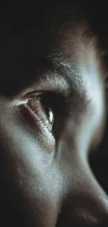 Close-up photo of a human eye in profile with dark, moody tones.