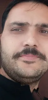 Close-up portrait of a man with facial hair, wearing a dark shirt.