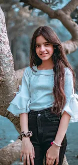 Mobile wallpaper featuring a young girl posing by a tree in a teal autumn setting.