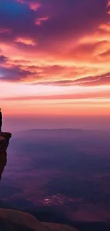 Silhouette on cliff at sunset with vibrant sky and clouds