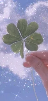 A hand holds a clover against a heart-shaped cloud in a shimmering blue sky.