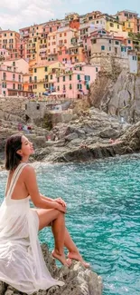 Woman sitting on rocks by a colorful seaside village.