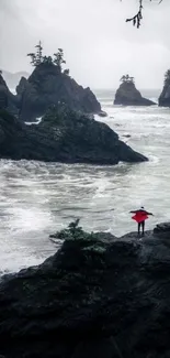 Person with red umbrella on rocky coast with ocean waves.