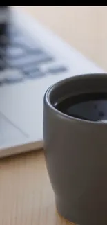 Coffee cup beside laptop on wooden desk.