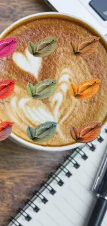 Coffee cup with autumn leaves and a notebook on a wooden desk.