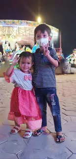 Two happy children at a colorful amusement park at night.