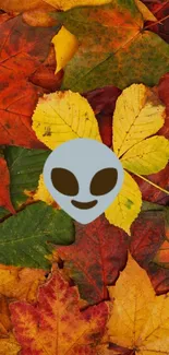 Mobile wallpaper with colorful autumn leaves and an alien emoji.