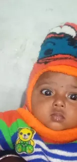 Adorable baby in colorful outfit with orange hat and big eyes.