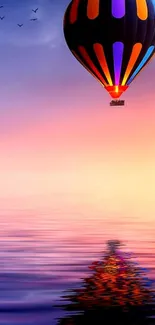 A hot air balloon floats over calm water at sunset, reflecting vibrant colors.