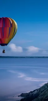 Colorful hot air balloon floating over a calm ocean under a blue sky.