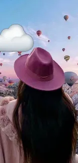 Person in a pink hat watching colorful hot air balloons in a blue sky.