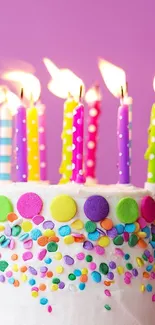 Colorful birthday cake with lit candles on purple background.