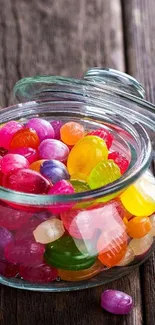 Glass jar filled with colorful candies on a rustic wooden surface.