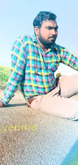 Man in colorful checkered shirt sitting outdoors on a sunny day.