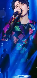 Singer in colorful jacket with blue concert lighting.