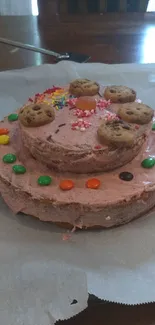 Mobile wallpaper of a colorful cookie cake with pink icing and assorted toppings.