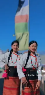 Two individuals in vibrant cultural attire with scenic backdrop.