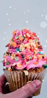 Hand holding a colorful cupcake with pink frosting and cereal decorations.